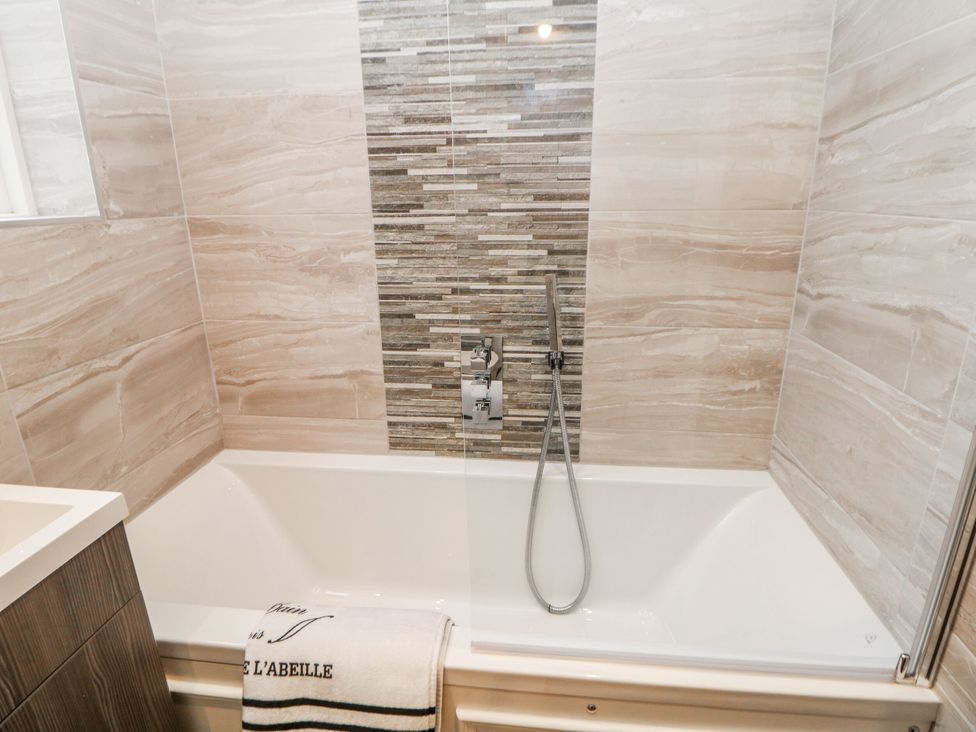 A bathtub with a shower and tile wall at Riber, Matlock Bath