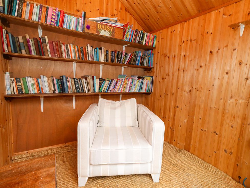 A reading room with a bookshelf and a white chair at Garden Retreat in Swanage