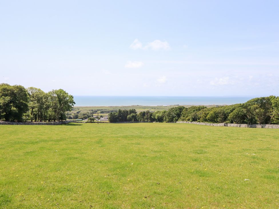 A scenic outdoor area with grass and trees overlooking the ocean at Ysgubor Newydd Parc Isaf Dyffryn Ardudwy
