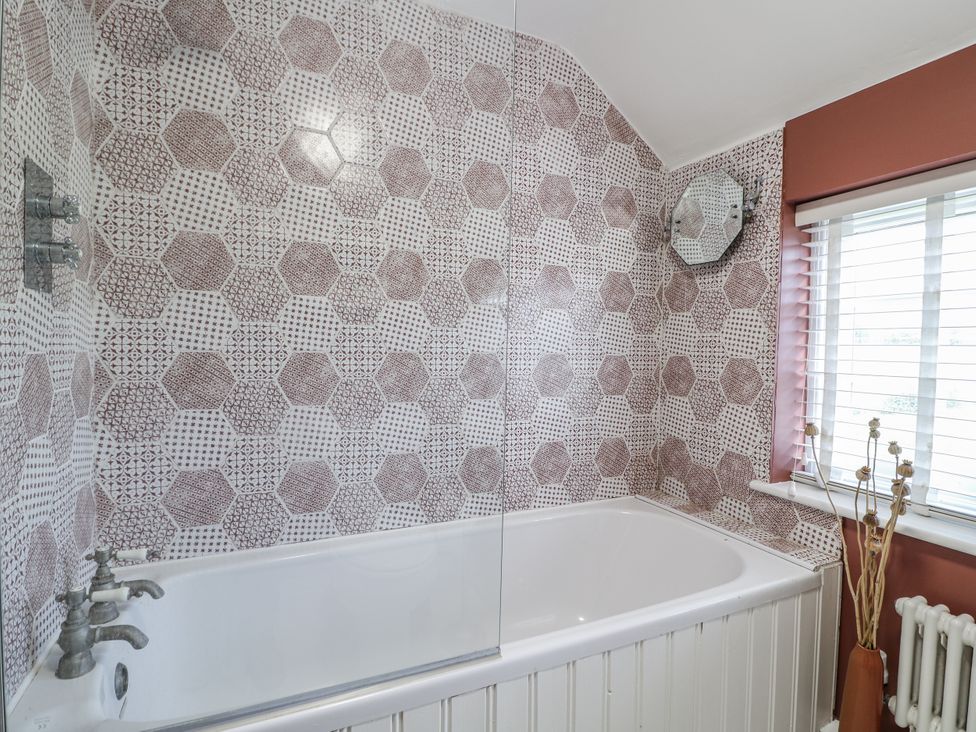 A bathroom with a bathtub surrounded by patterned tiles at Gapstile in Abbots Bromley