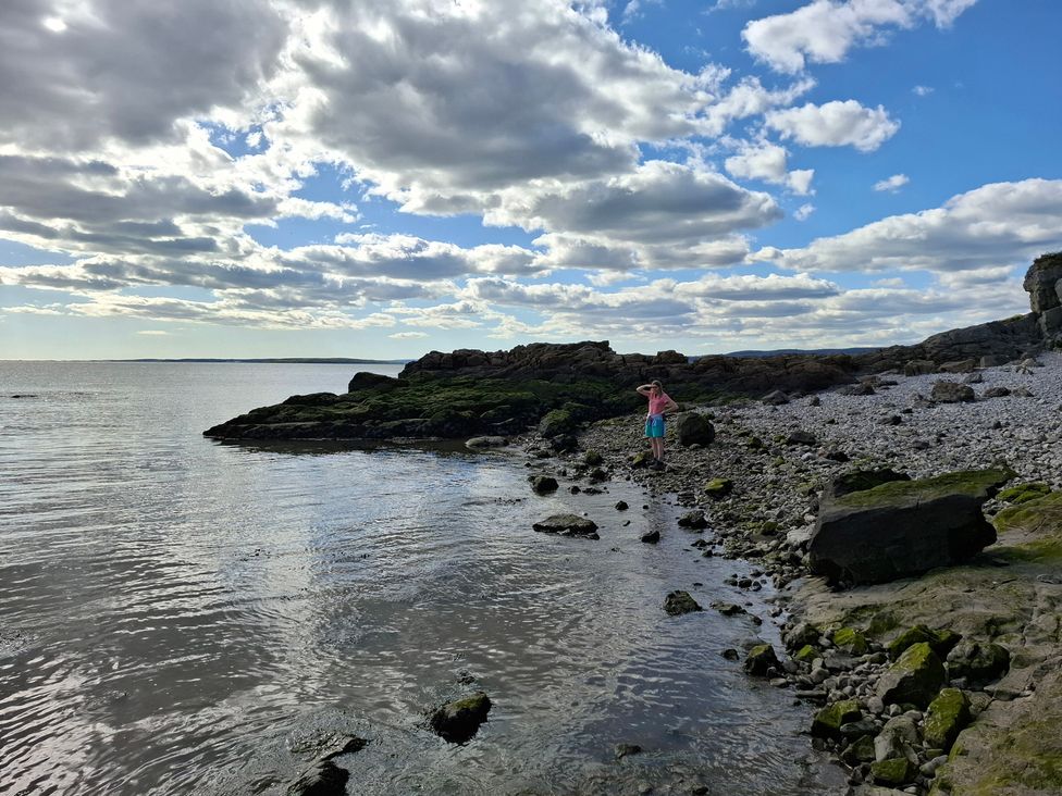A shoreline with rocks and a person standing by the water at 28 Rock Villas Silverdale