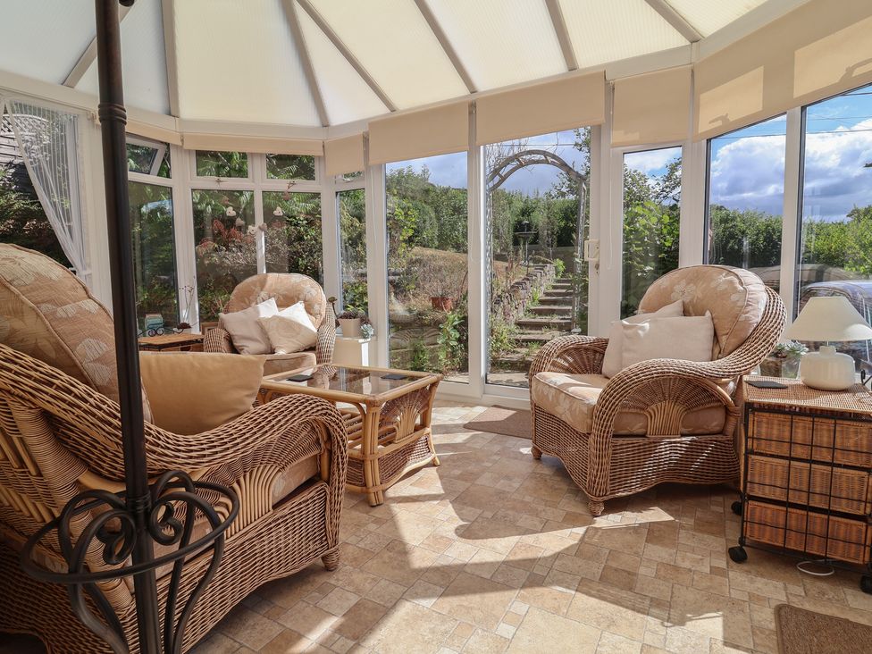 A conservatory with rattan chairs and a coffee table at Little Willesleigh in Goodleigh near Barnstaple