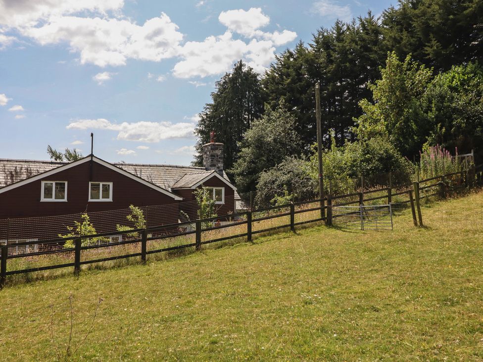 A building with a fence and trees in a field at Bryn Y Garreg Cottage - The Wireless Free Farm Llangadfan near Llanwddyn