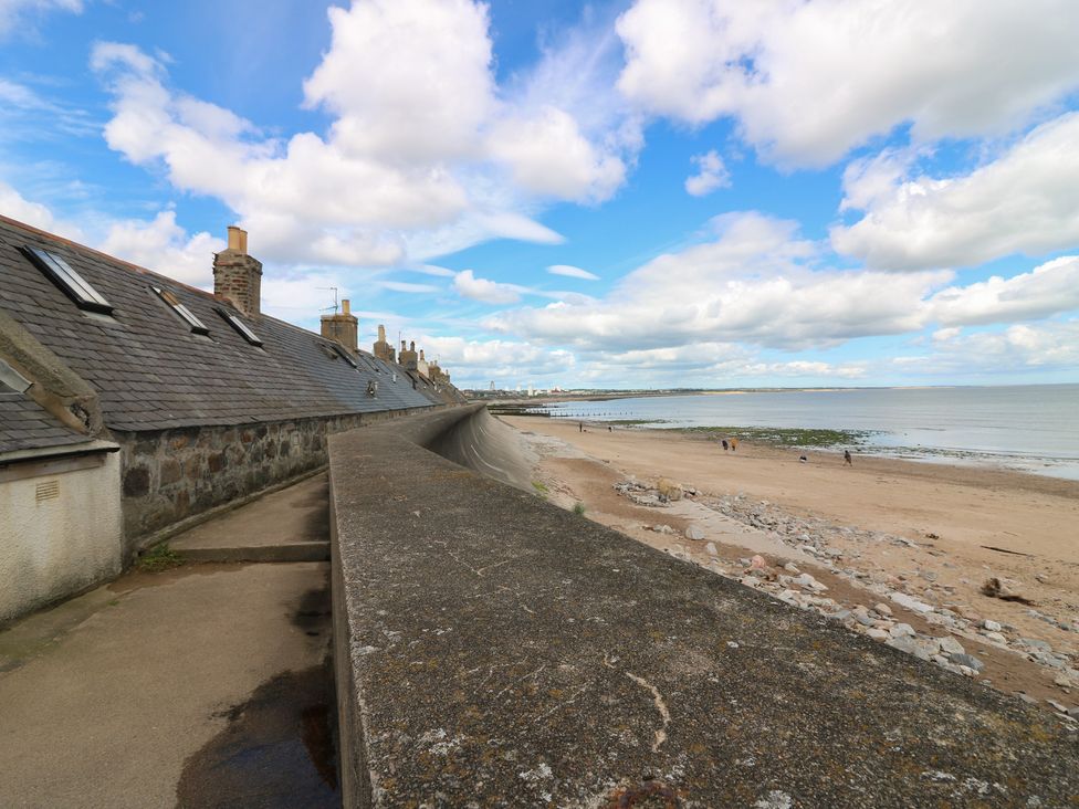 A beach with a pathway and clouds at Footdee Cottage in Aberdeen