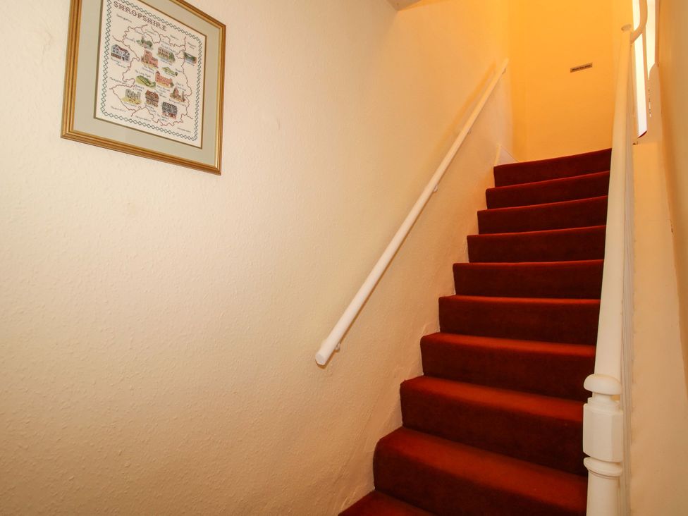 A staircase with red carpet and a framed picture at Beach Farmhouse in Bishops Castle