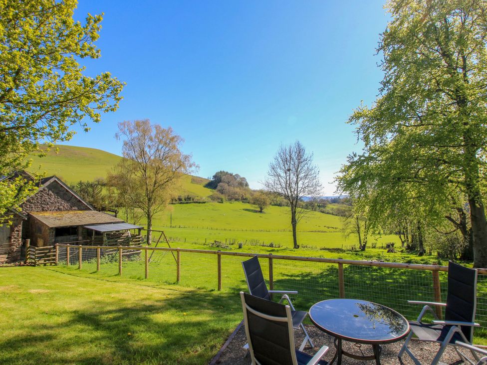 A garden with chairs and a table overlooking a field at Beach Farmhouse in Bishops Castle