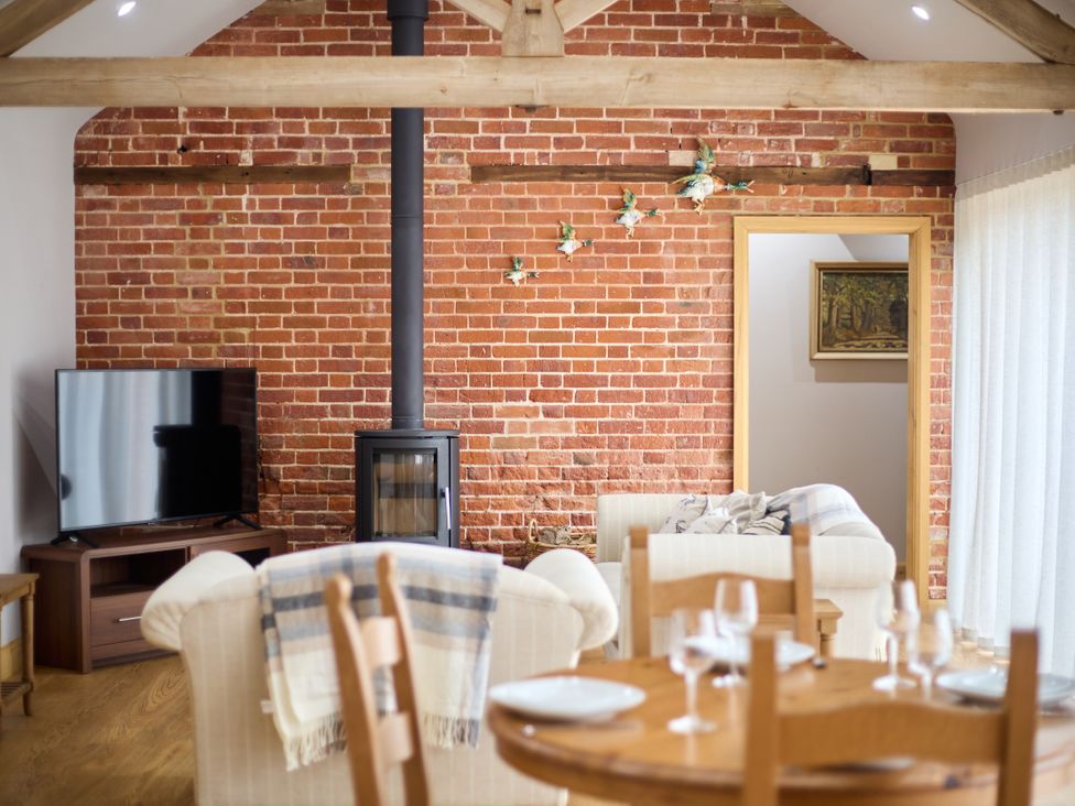 A living room with a television, wood stove, and dining table at The Saddlery in Norwich