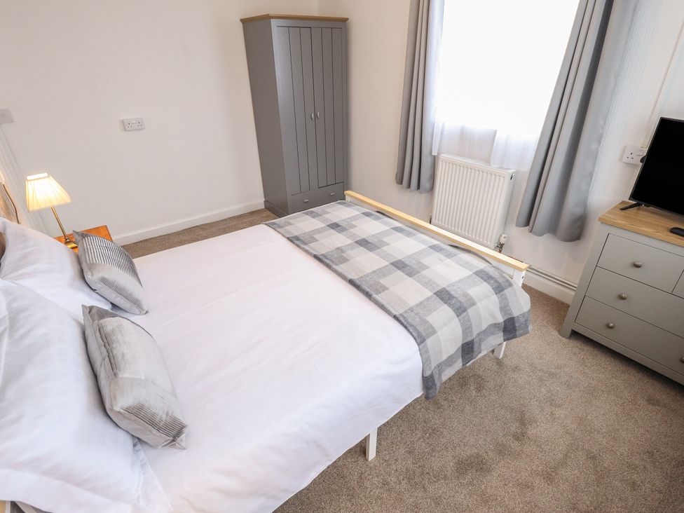 A bedroom with a bed, wardrobe, television and curtains at Orby Cottage in Chapel St Leonards