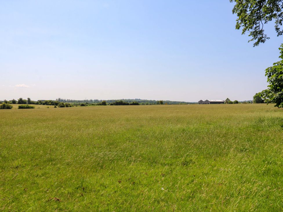 A green field with trees and farm buildings at Little Yeat Farm in Aylesbury