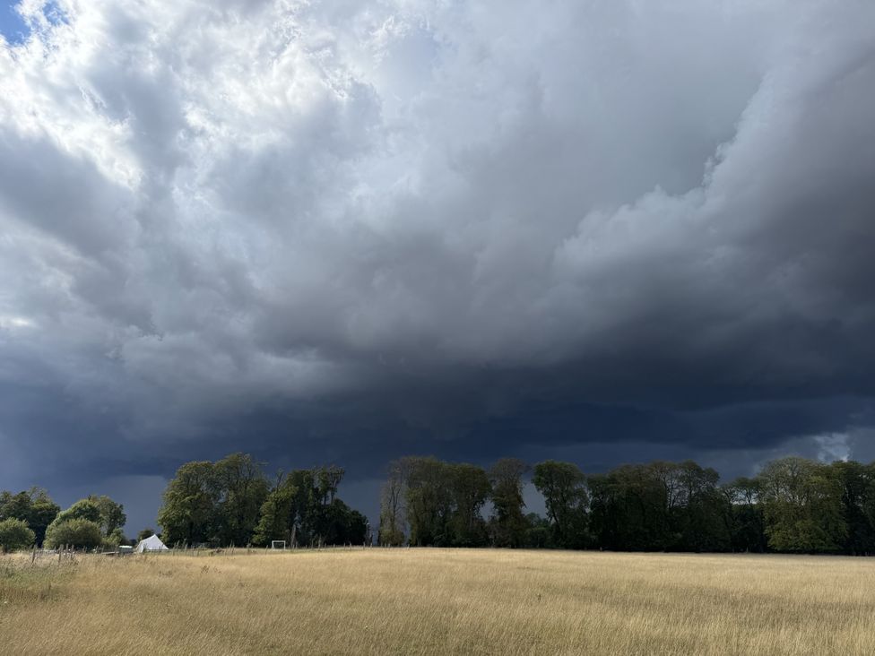 A field with trees and dark clouds at Number 3 The Barn House Woodham