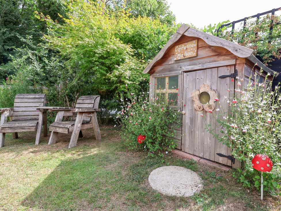 A children's playhouse and wooden chairs in a garden at The Corner House Ufford near Woodbridge
