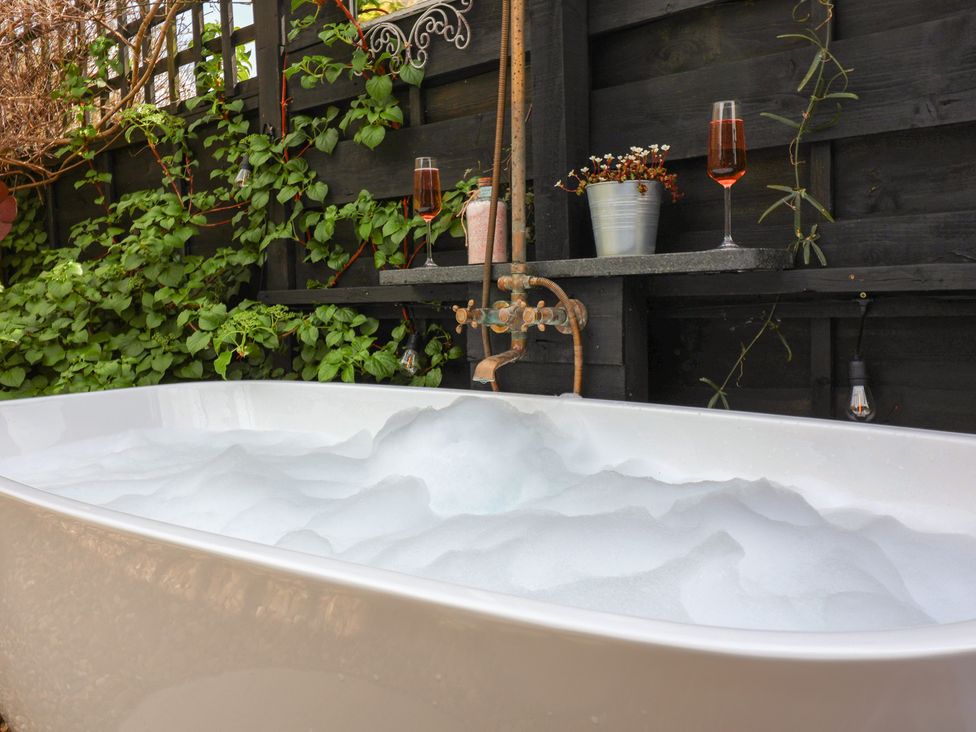 A bathtub with bubbles near plants and glasses at The Corner House in Ufford near Woodbridge