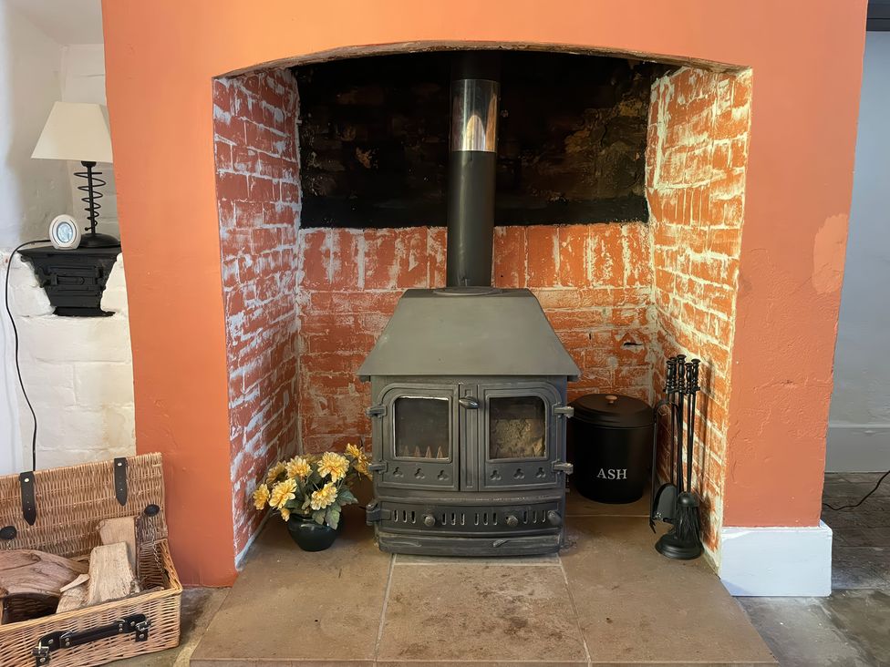 A fireplace with a wood stove and a basket of logs at Vinney Cottage in Owermoigne