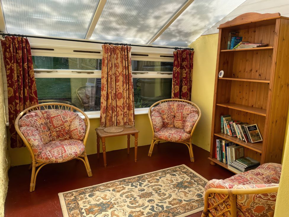 A conservatory with rattan chairs and a bookcase at Vinney Cottage in Owermoigne