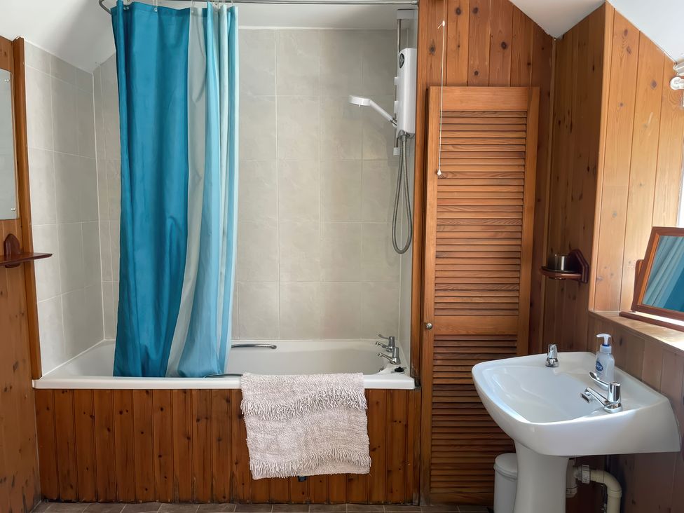 A bathroom featuring a bathtub with shower curtain and sink at Vinney Cottage in Owermoigne
