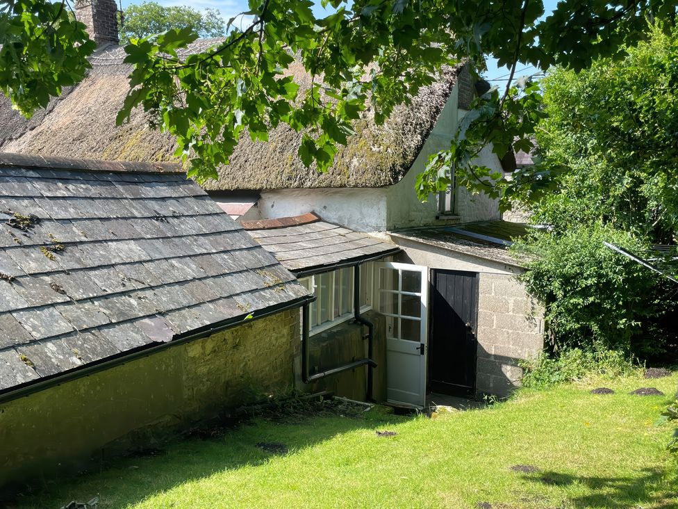A garden view of a stone building with a thatched roof at Vinney Cottage in Owermoigne