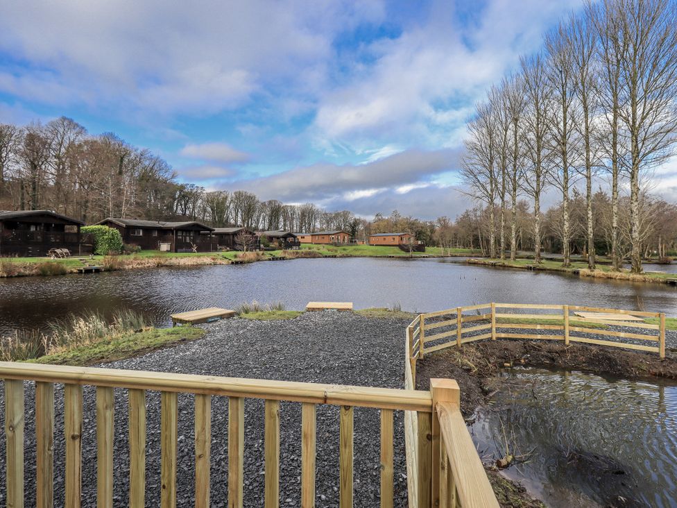View of a pond with log cabins and trees at Lakeside Lodge Bowland Lakes Leisure Village near Garstang