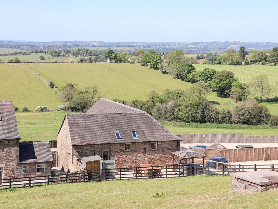 A stone cottage with a fenced patio and cars parked nearby in a rural setting at Parlour Barn in Leek
