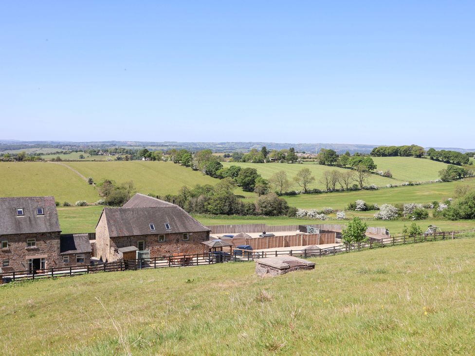 Stone buildings with fences and a large fenced area surrounded by grassy fields and trees at Parlour Barn in Leek