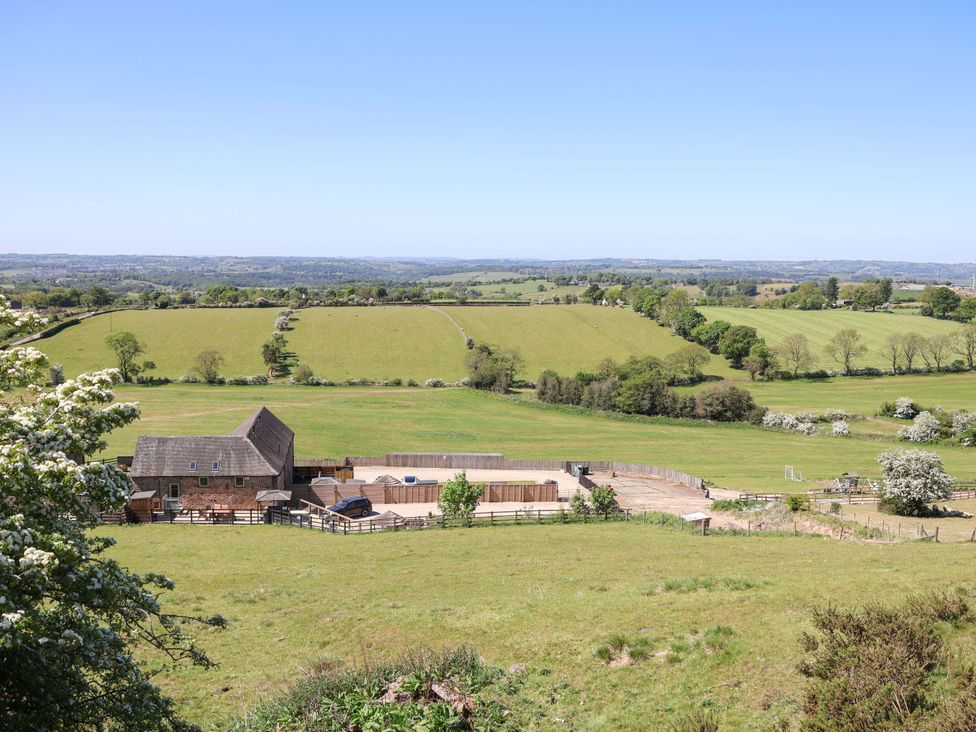 A countryside view with a barn building fenced enclosures and rolling green fields at Parlour Barn in Leek