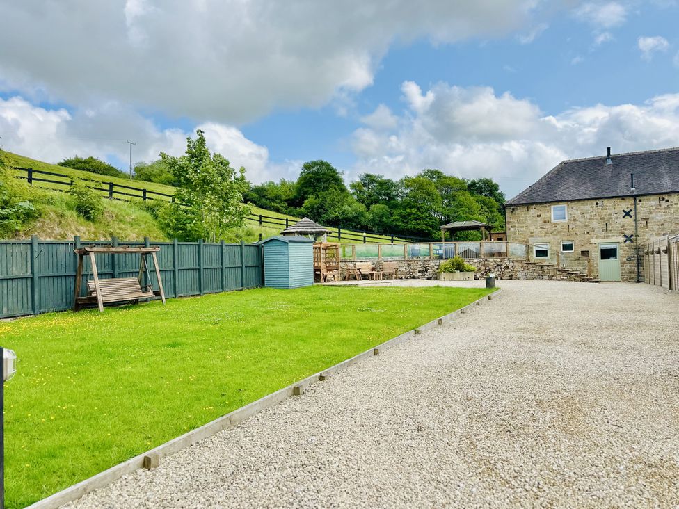 A fenced garden with swing set, gazebo and patio area at Parlour Barn in Leek