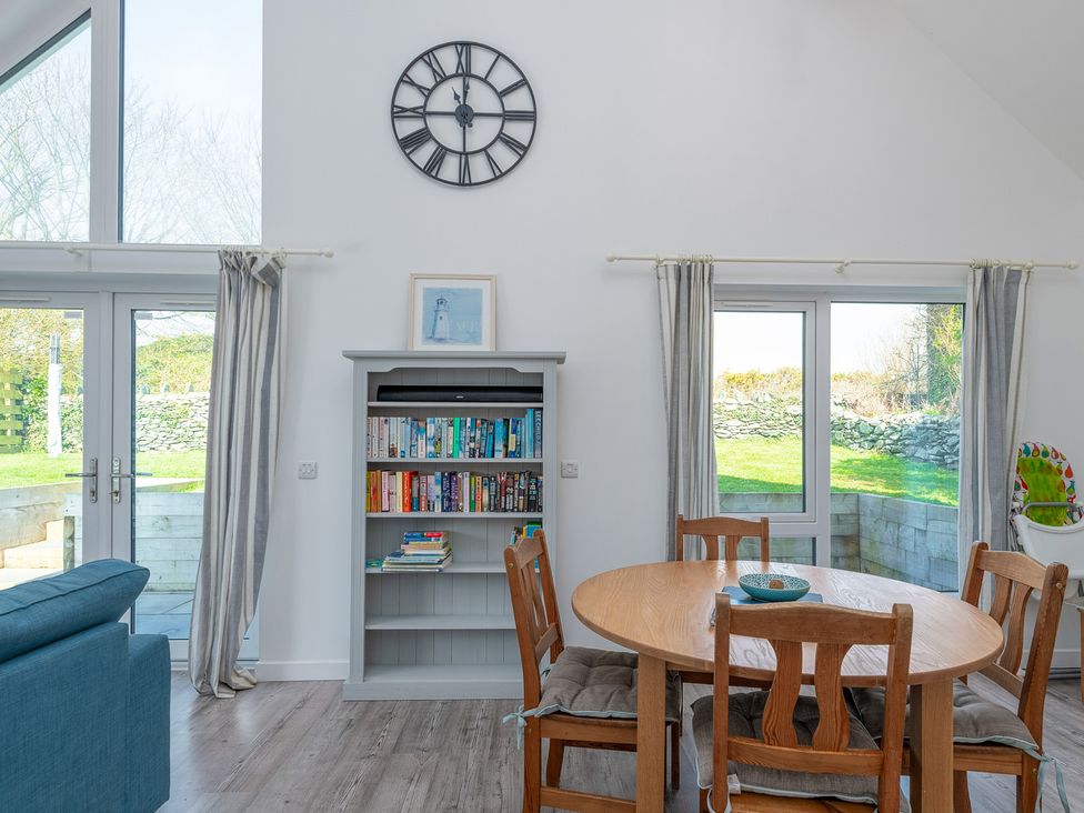 A dining room with a table and books on a shelf at Moranedd Bach in Holyhead