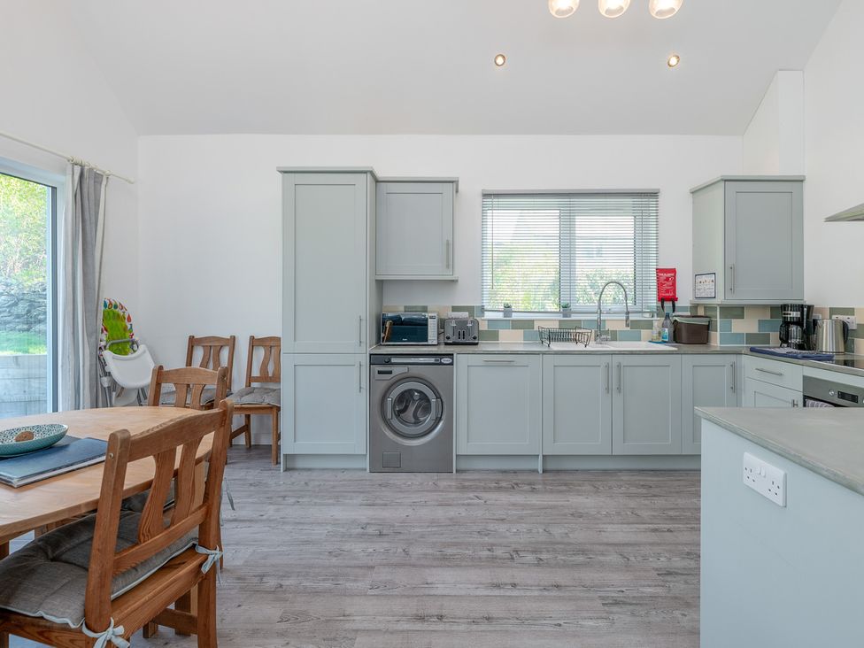 A kitchen with cabinets and dining table at Moranedd Bach in Holyhead