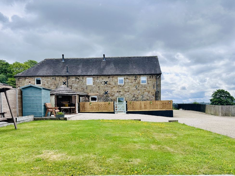 A stone house with a pitched roof a small blue shed a wooden fence a gravel driveway and a grassy lawn at Pastures Barn in Bradnop near Leek