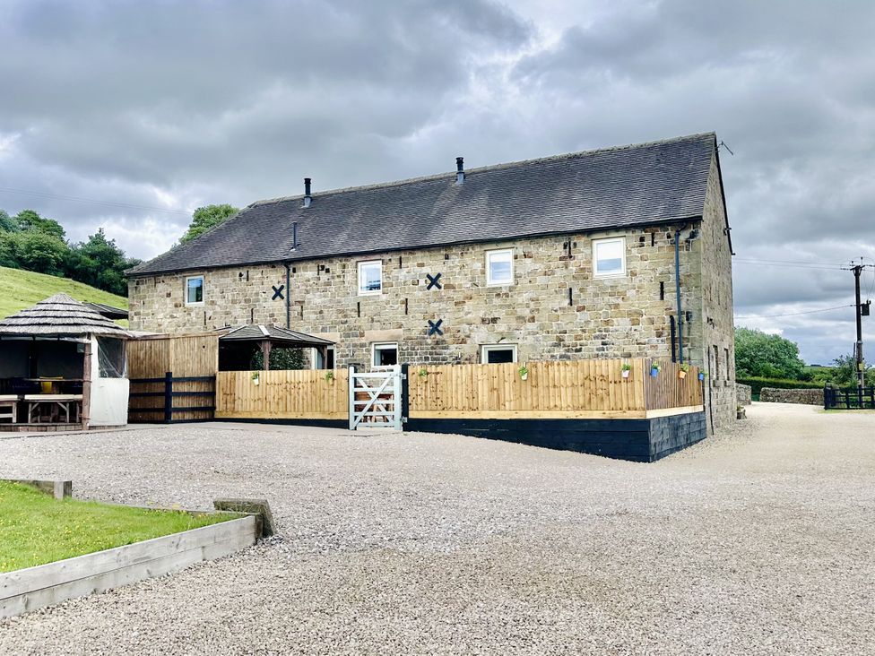 A stone barn with a gravel driveway and fenced patio area with a wooden gazebo at Pastures Barn in Bradnop near Leek
