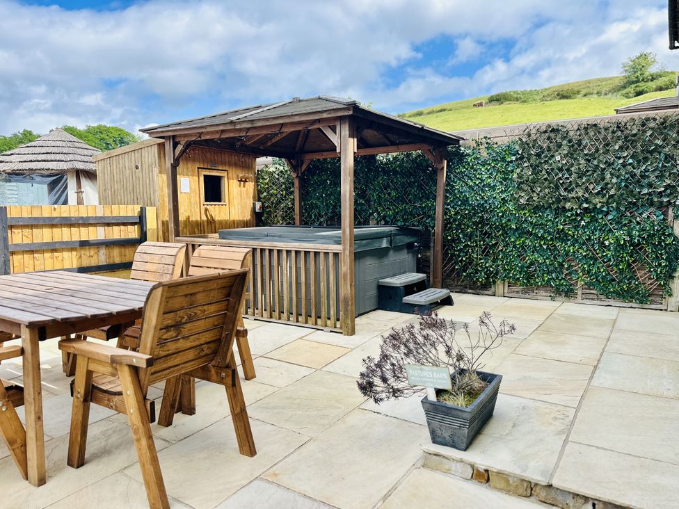 An outdoor patio with wooden table and chairs a hot tub under a wooden gazebo and a potted plant at Pastures Barn Bradnop near Leek
