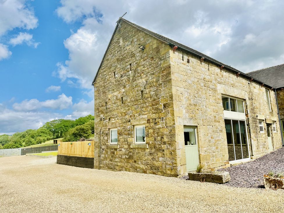 Exterior of a stone barn building with gravel ground and wooden fencing at Pastures Barn in Bradnop near Leek