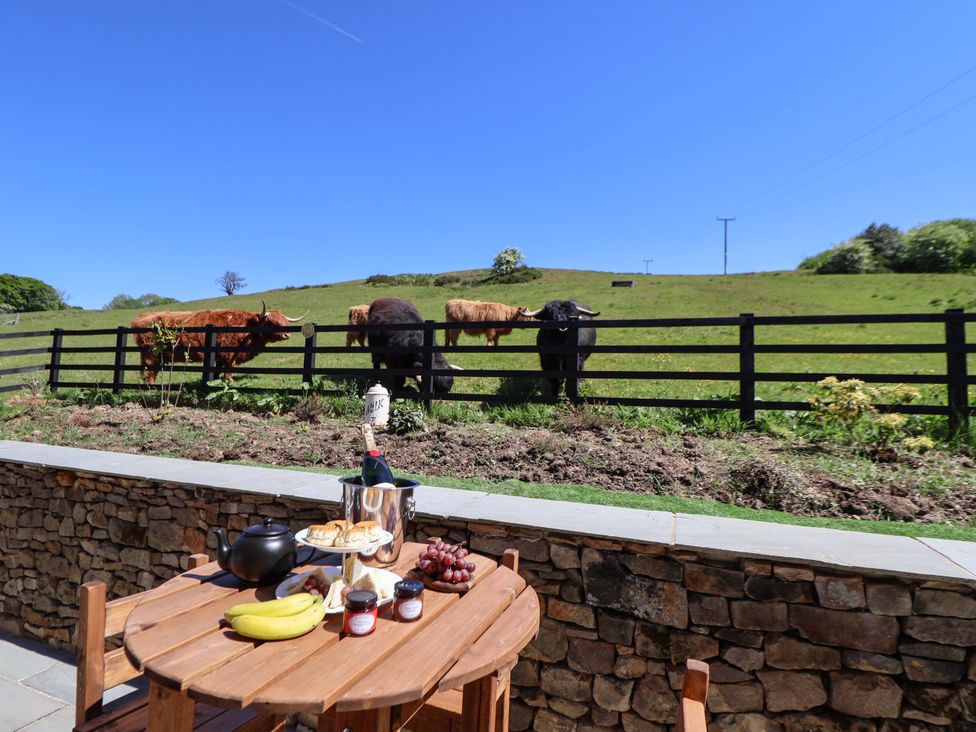 A wooden table with breakfast items outside with cows behind a fence at HollyDale in Bradnop near Leek