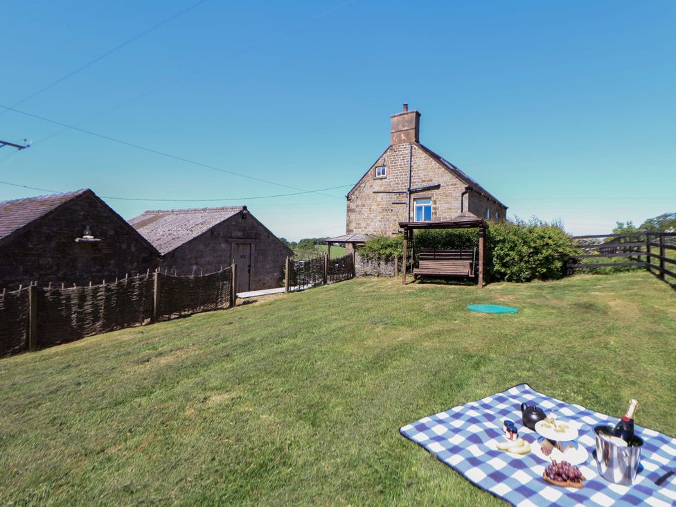 A stone house with two outbuildings a wooden bench swing and a picnic setup on a blanket on the grass at HollyDale in Bradnop near Leek