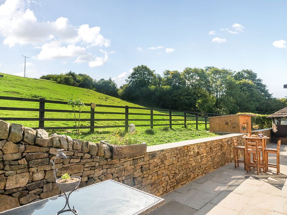 An outdoor area with a stone wall, table, and chairs at HollyDale in Bradnop near Leek