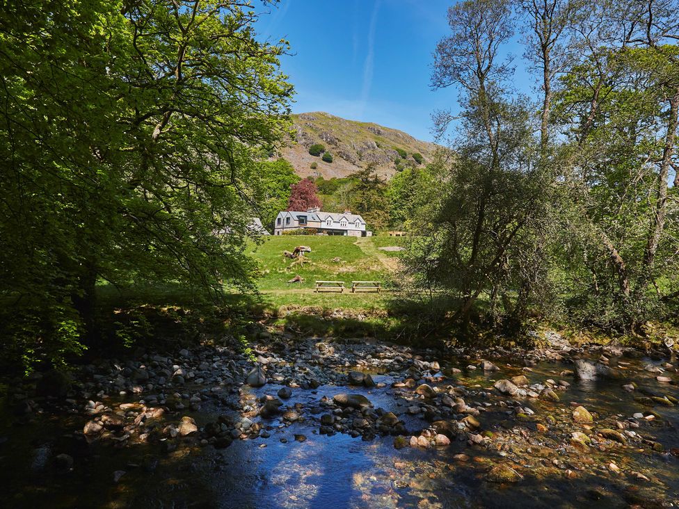 A stone house behind green grass with two picnic benches by a rocky stream surrounded by trees at Eskdale Retreat in Boot