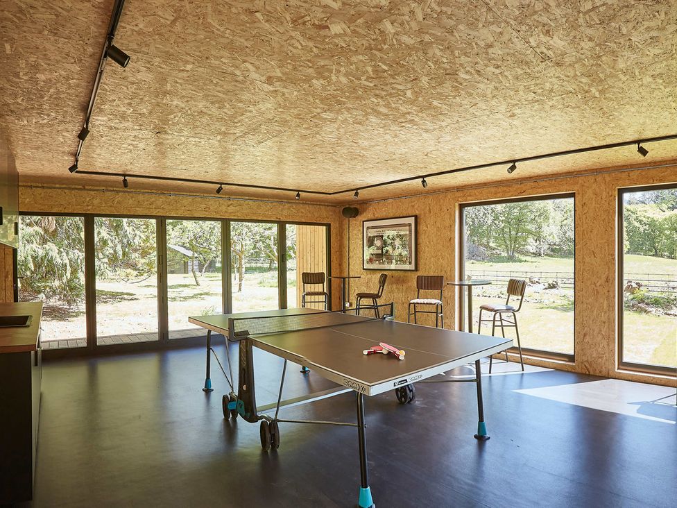 A room with a table tennis table stools and large windows showing an outdoor area at Eskdale Retreat in Boot