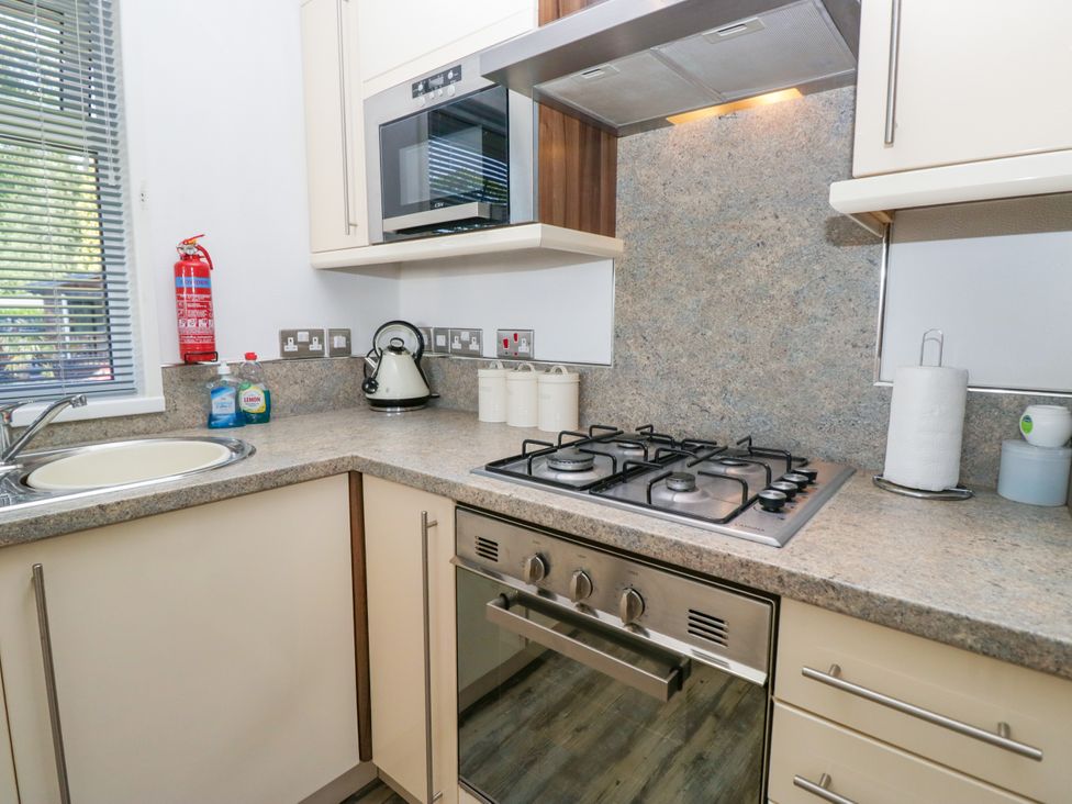 A kitchen with a sink, gas stove, and microwave at Dovedale Lodge in Troutbeck Bridge