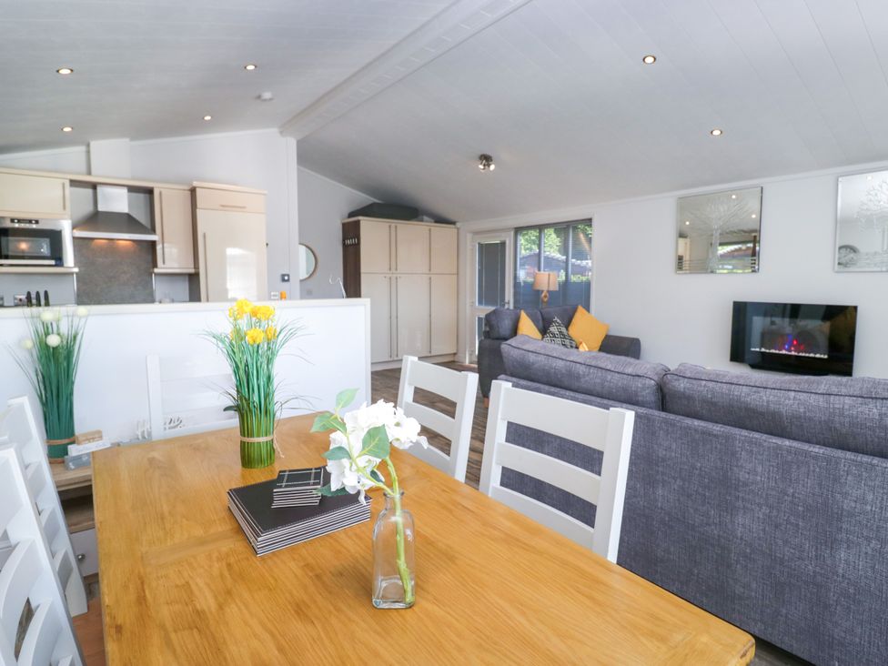 A dining area with a wooden table and kitchen appliances at Dovedale Lodge in Troutbeck Bridge