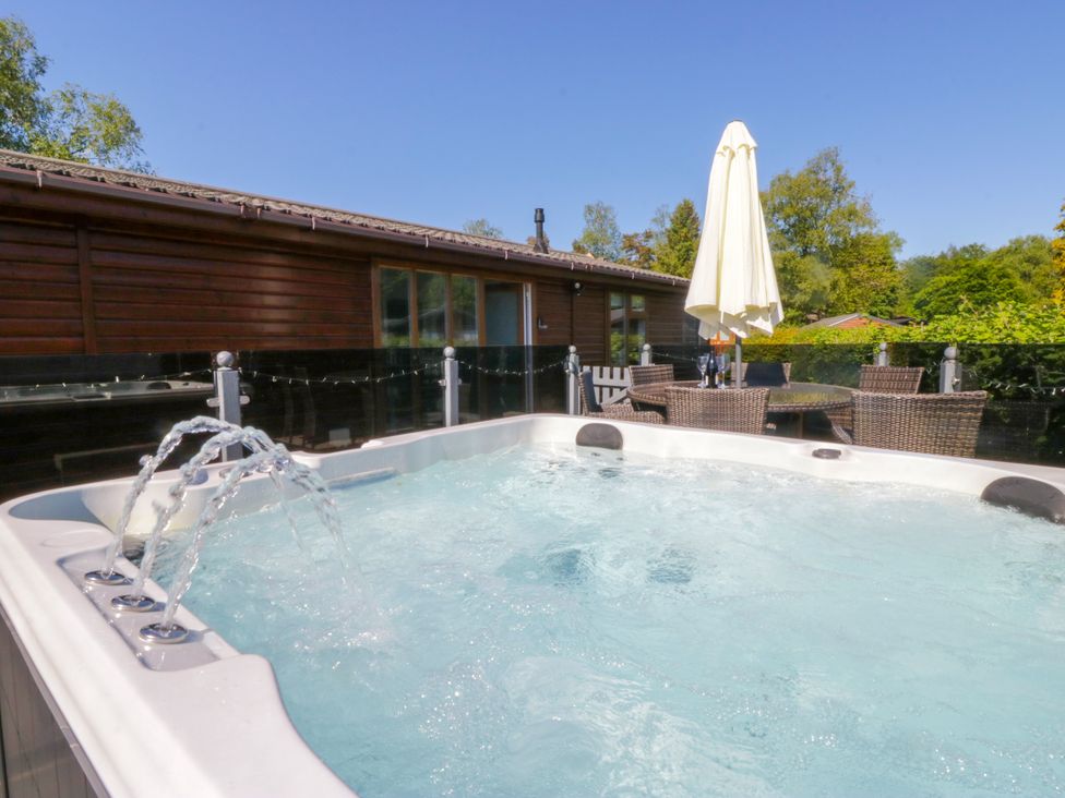 A hot tub with outdoor furniture and an umbrella at Dovedale Lodge in Troutbeck Bridge