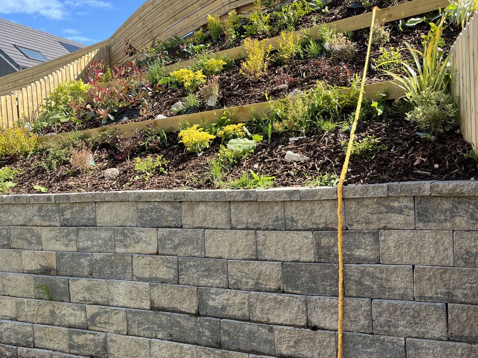A garden with plants and a stone retaining wall at Golygfa Gele in Llanddulas