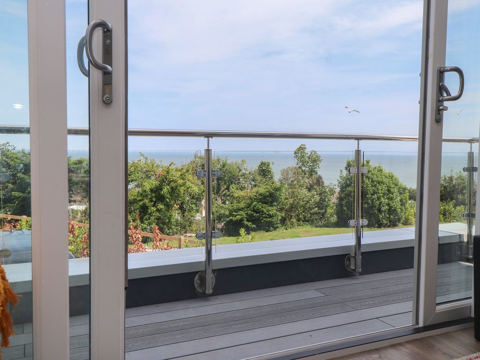 An outdoor area with a glass door and railing overlooking the sea at Golygfa Gele in Llanddulas