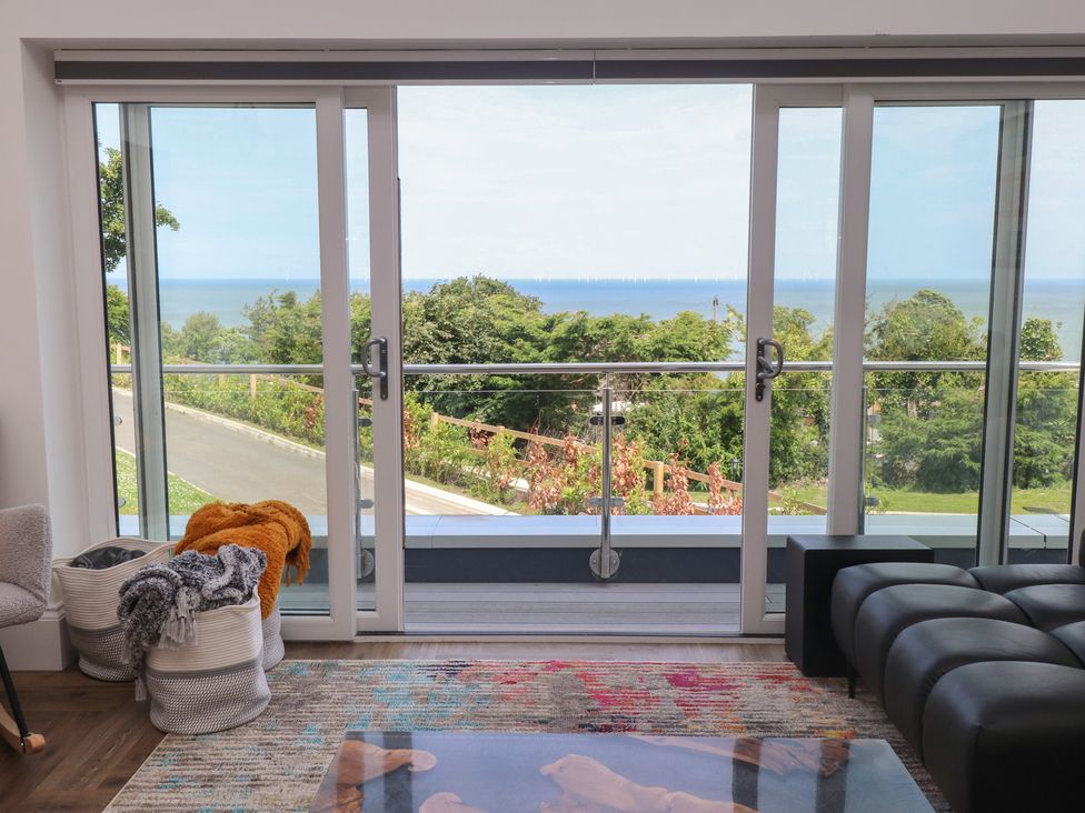 A living room with sliding glass doors opening to an ocean view at Golygfa Gele Llanddulas