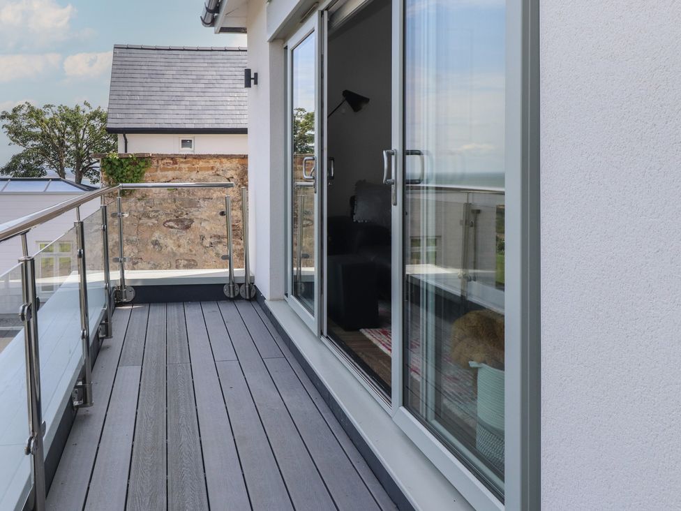 A balcony with wooden flooring and glass railing at Golygfa Gele in Llanddulas