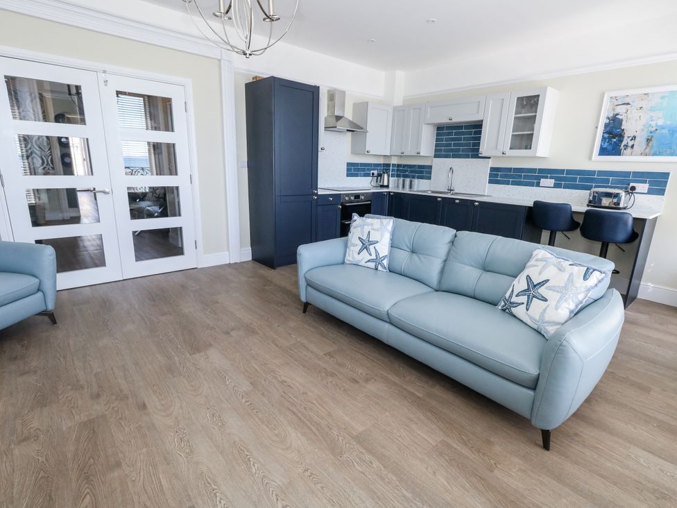 A living room with a blue sofa and kitchen area at Apartment 1 Weymouth