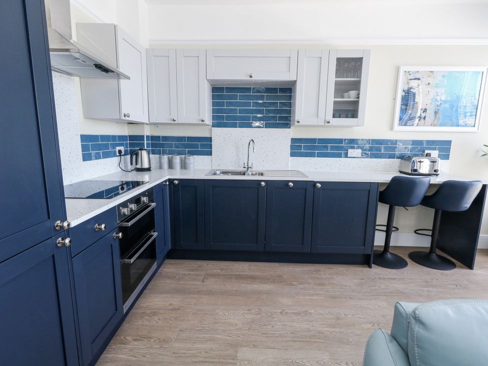 A kitchen with appliances and bar stools at Apartment 1 in Weymouth