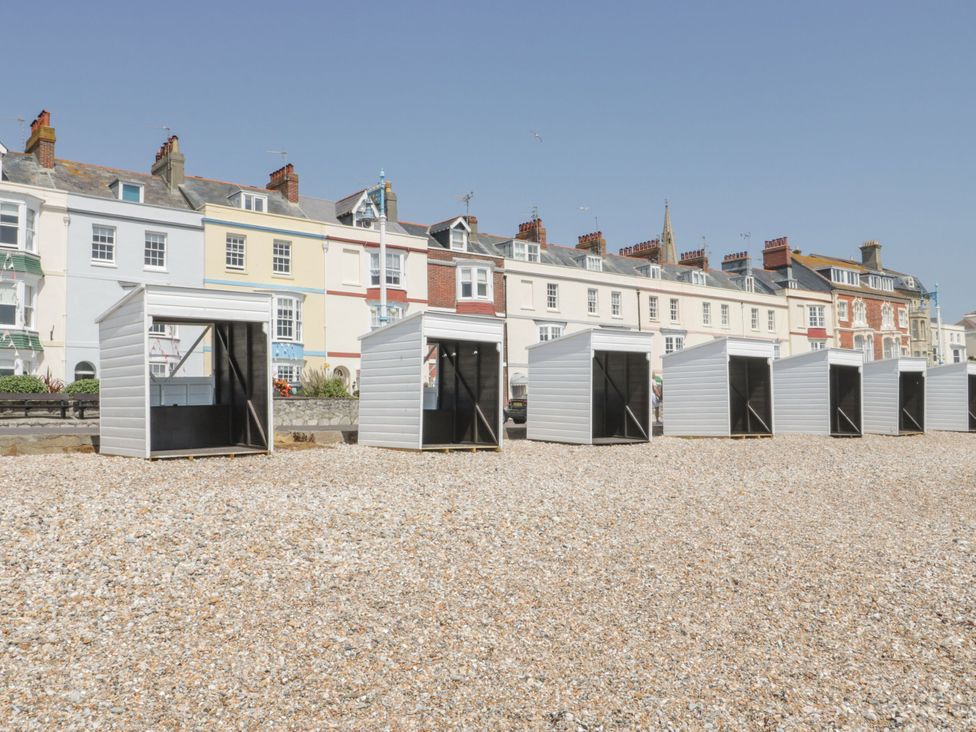 A row of beach huts on gravel with buildings in the background at Apartment 2 Weymouth