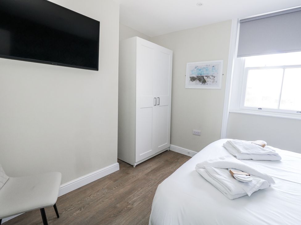 A bedroom with a bed, wardrobe, television, and a chair at Vista Mare 2 in Weymouth