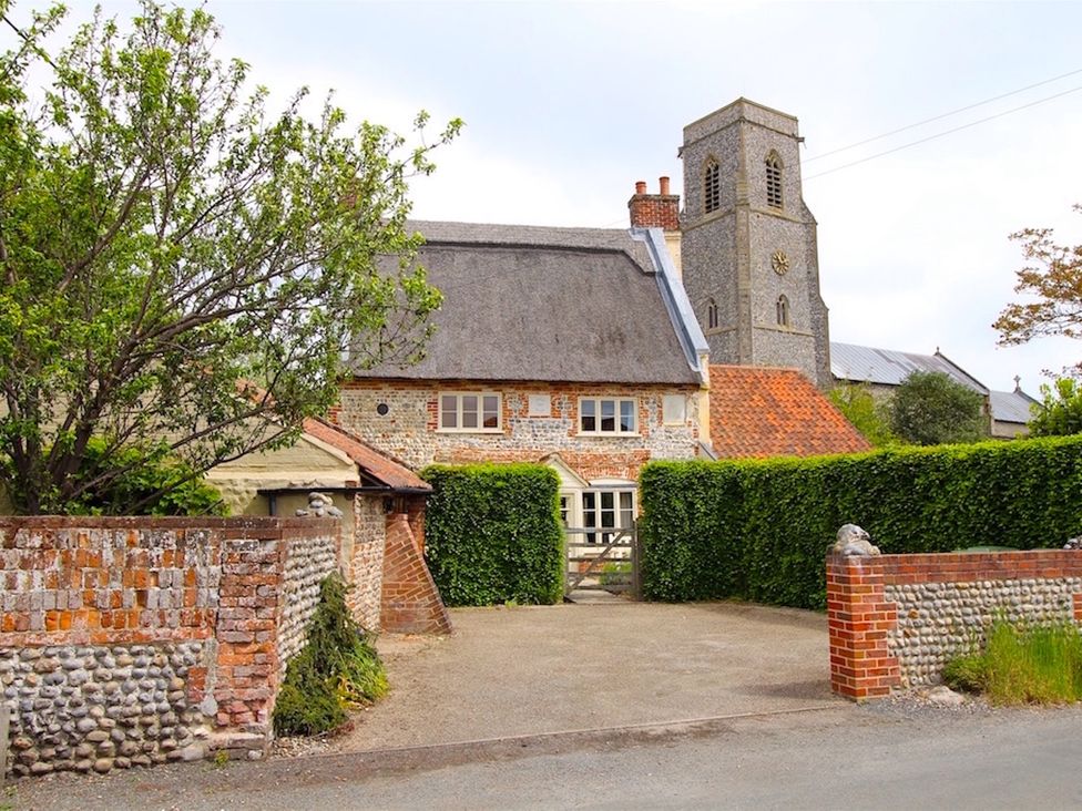 A cottage with a thatched roof and church tower at Thatch Cottage in Trunch