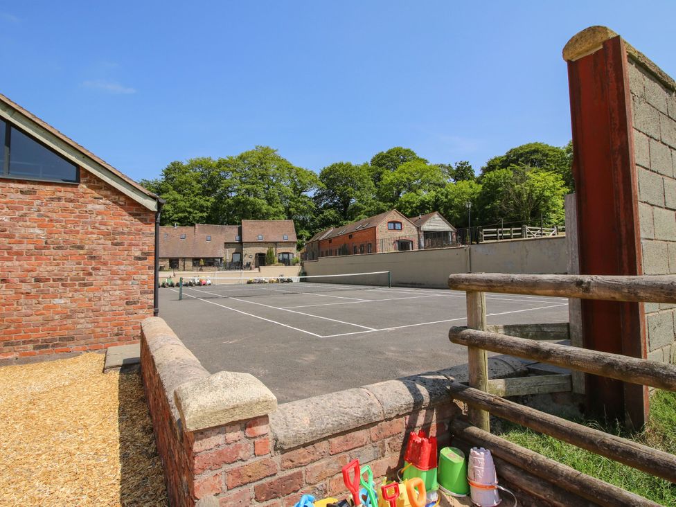 A tennis court with surrounding buildings at Upper Home Farm near Cardington