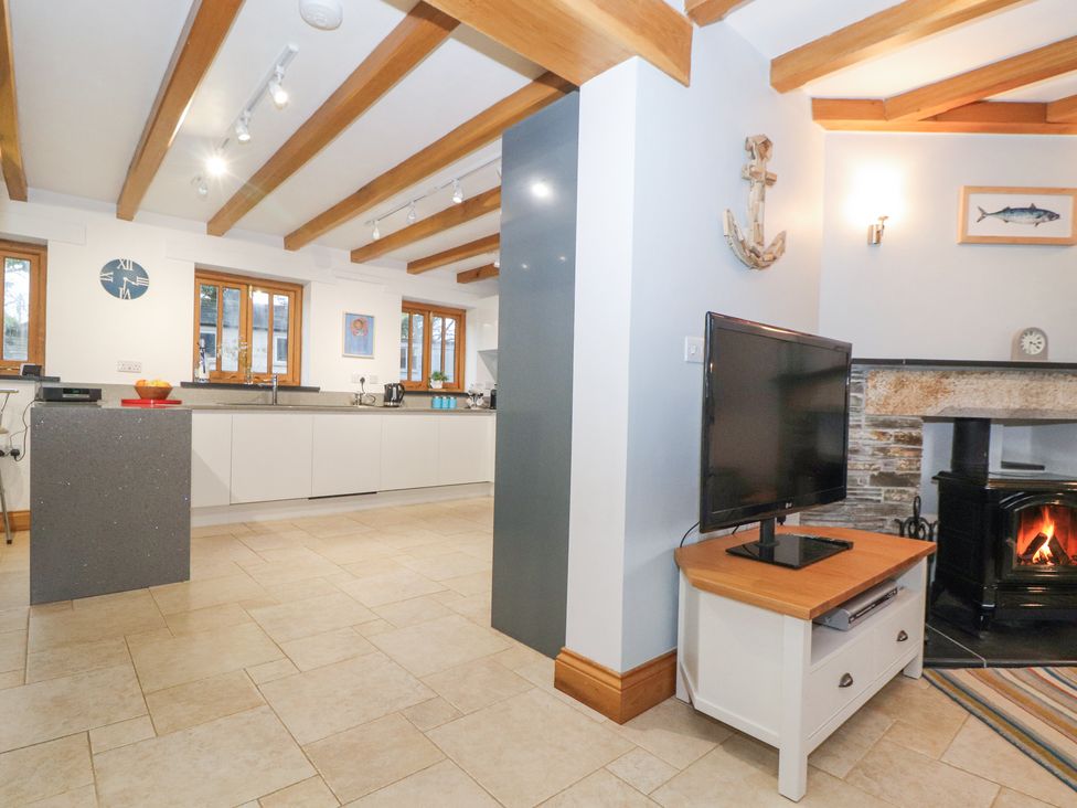 An open kitchen and living area with wooden ceiling beams a television on a stand and a fireplace at Splatt Barn Rock